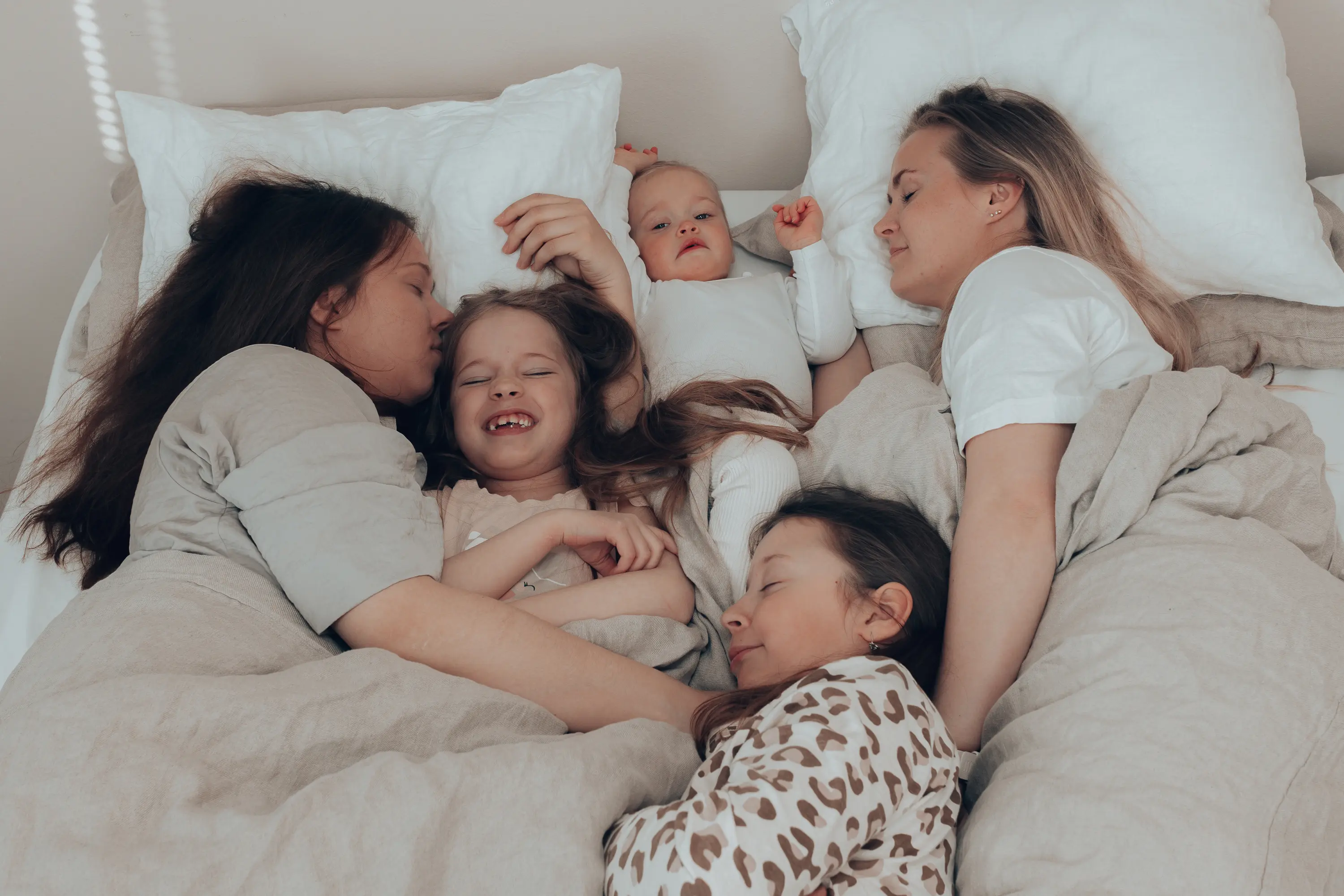 Kaksi naista makaamassa sängyllä kolmen lapsen kanssa