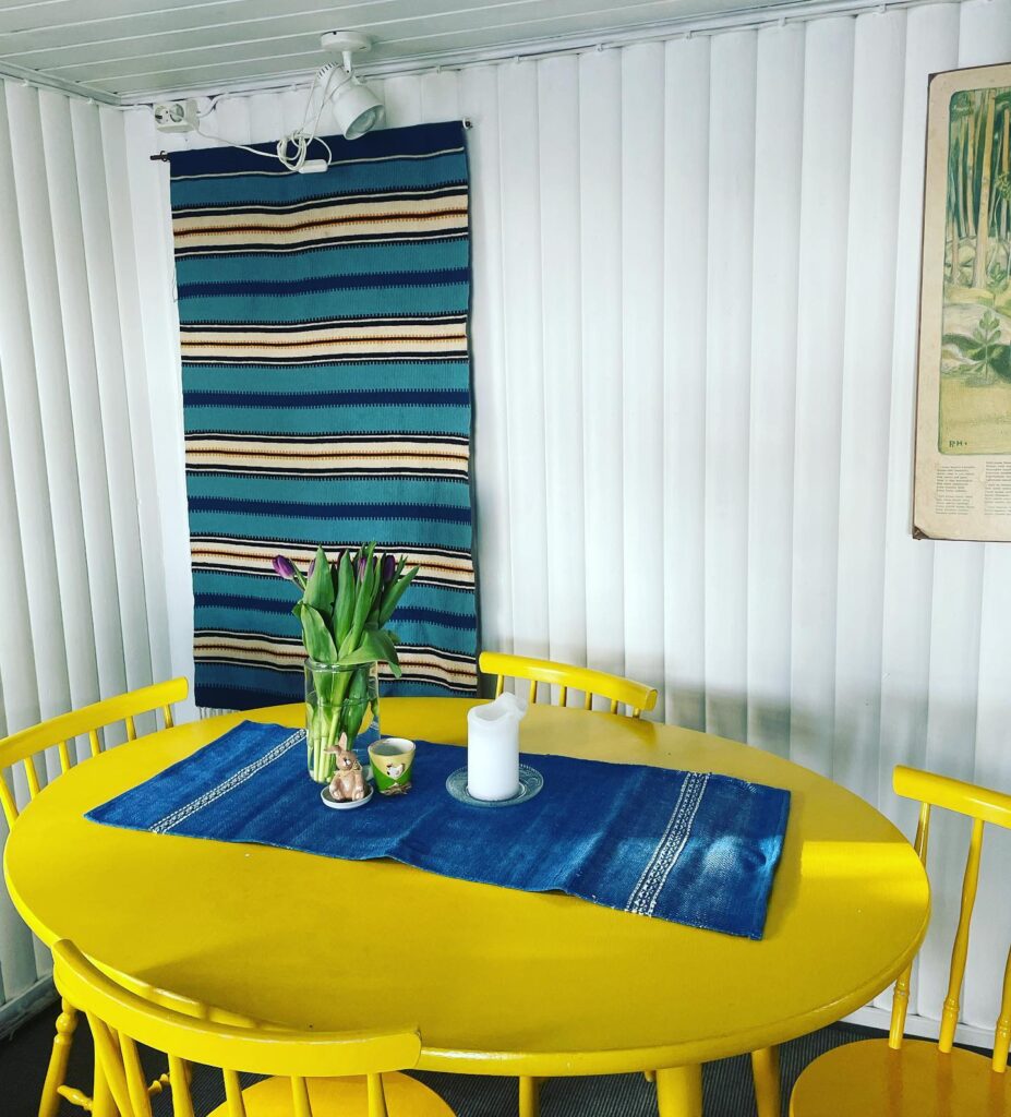 Iloisen värinen pöytä ja perinteikäs raanu seinällä.